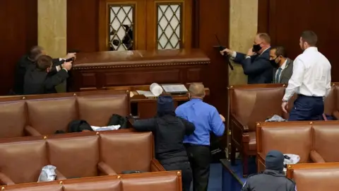 Getty Images Capitol police point guns at a protester from inside the House chamber