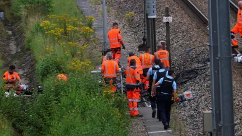 REUTERS/Brian Snyder Pracownicy kolei i funkcjonariusze organów ścigania SNCF pracują na miejscu, w którym sabotażyści zaatakowali sieć kolei dużych prędkości we Francji, podejmując szereg skoordynowanych działań, które spowodowały poważne zakłócenia przed ceremonią otwarcia Igrzysk Olimpijskich w Paryżu w 2024 r. w Croiselles.