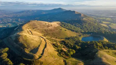 Getty Images The Malvern Hills with the Iron age hill fort in the foreground. The sun is shining over the landscape in the aerial image.