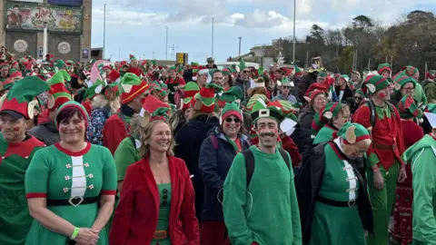 BBC A group of people wearing red, white and green elf costumes.