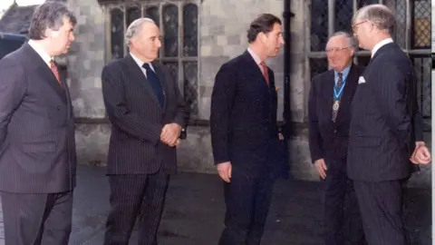 Wilton Park Four men in suits standing outside a stately home.