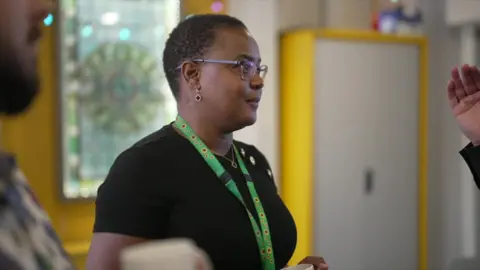 BBC Violet Gutu wears a green lanyard and black t-shirt studded with three gold buttons. She is side on to the camera