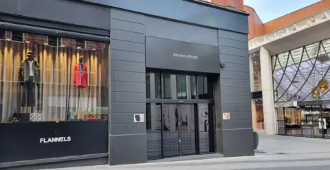 An exterior shot of The Man Behind the Curtain in central Leeds: a black-fronted building with double glass doors.