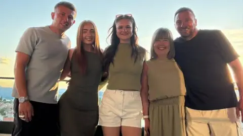 John Heeps A family on holiday smiling with a sunset behind them