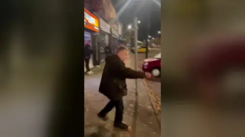 Screengrab of Mike Amesbury pointing at unseen person on a street outside shops at night