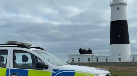 Guernsey Police Image of police car parked next to the Alderney lighthouse.
