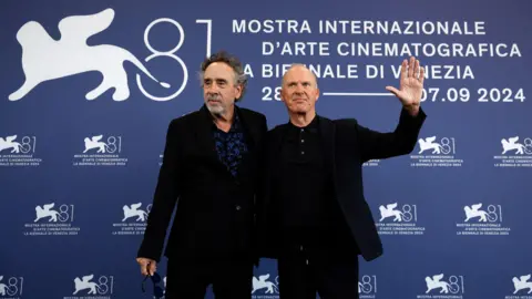 Reuters Tim Burton and Michael Keaton on the red carpet at the 81st Venice Film Festival both men are wearing black and Keaton has one arm around Burton and the other raised in the air waving