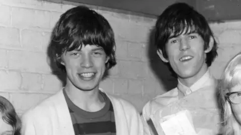 Mick Jagger and Keith Richards - both smiling. A black and white photo from 1964