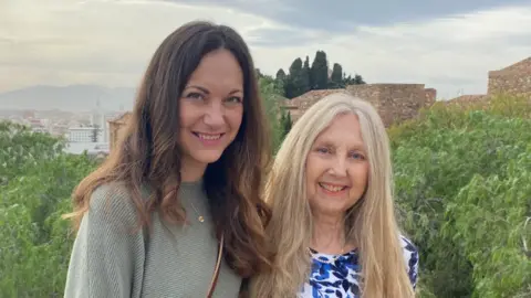 Supplied Sophie, with long dark hair, stood next to her mother Ellen, who has light, long hair. Both are smiling and stood in front of a city view.