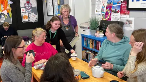 Sophie is pictured serving a number of women who are seated at a table drinking tea. She has a helper behind her.