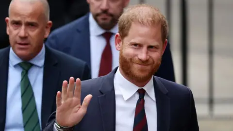 EPA Prince Harry, wearing a dark suit and striped tie, waving to cameras
