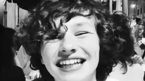 Family handout A black-and-white photograph of Gabriel who is smiling in a busy restaurant. He has long, dark, curly hair.