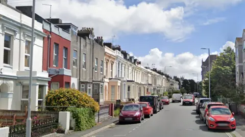 Google image of North Road West in Plymouth. Terraced properties line either side of the street. Cars are parked on both side of the road.