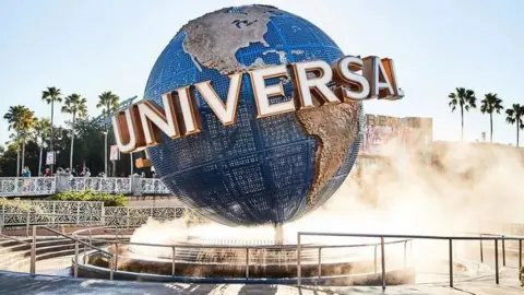 Universal Studios Globe with the word Universal written across it. It is sat on a fountain and misty water is coming upwards around the blue and brown globe. 