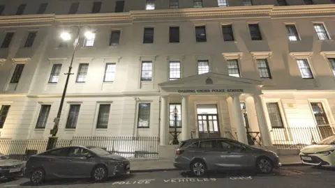 Getty Images An exterior view of Charing Cross Police Station at night: a white stucco neo-classical building with a four-pillared portico over the entrance and the Met Police's crest above the door.
