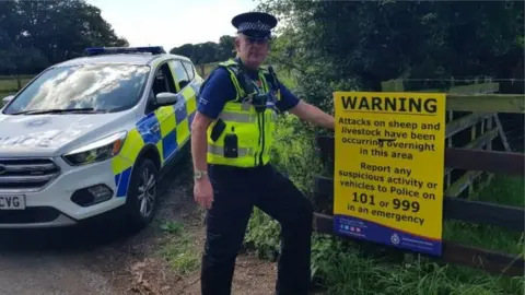 Northamptonshire Police Police Officer with sign on a gate