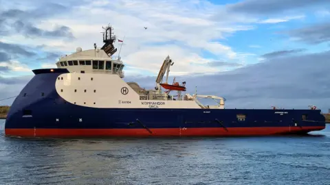 Hays Ships The blue, white and red-painted Kommandor Orca at sea. A deck crane is visible halfway along the ship in front of the cargo deck.