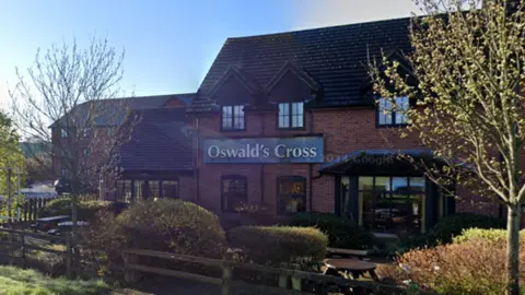 Google The front of a brown brick building with the words Oswald's Cross on a green sign in gold lettering