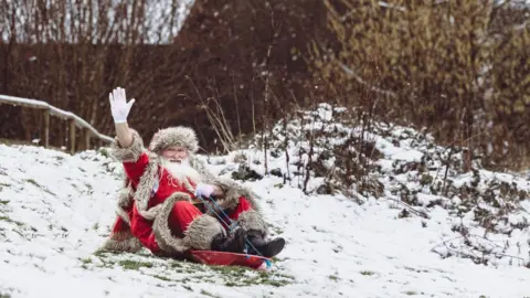 Bluestone National Park Resort Santa on small red toboggan coming down a hill and waving
