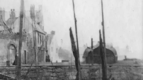 A very old image of the Eyemouth harbour. through all the masts the Old Coble House is visible with an upturned hull of a boat as its roof