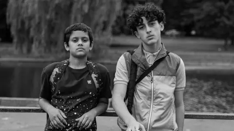 Two young people stand side by side in a black-and-white still from the film Ish.
