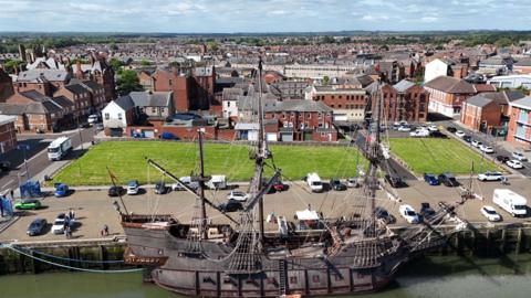 A tall ship moored up at the harbour at Blyth with the town stretched out behind