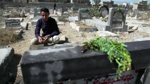 Awab sits beside his father's grave at a cemetery in Sanaa, Yemen