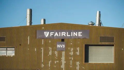 Ant Saddington/BBC A yellow corrugated metal building with a "Fairline" logo on a black banner.