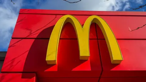 A red building with a yellow letter M on it. It is the logo for McDonald's.