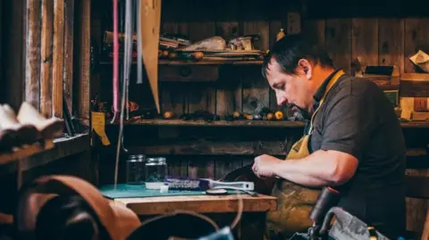 Amgueddfa Cymru Geraint Parfitt in his workshop. He is sitting in front of a wooden table with a brush on top.