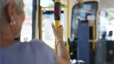 Getty Images A senior woman on a bus holds a bar with a stop button on it