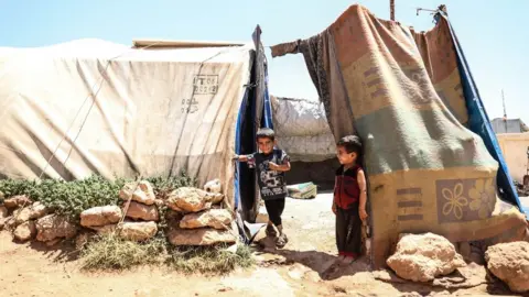 Anadolu Agency Syrian children sile at a camp for displaced people in opposition-held Idlib province, Syria (6 July 2023)