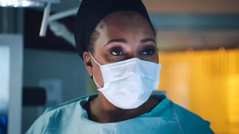 BBC Max McGerry (Jo Martin) in a mask in Holby City