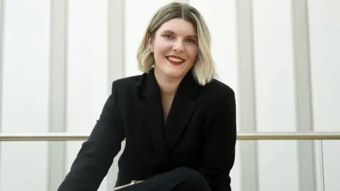 Irina Birt-Wiggins Jess Warren in a black suit