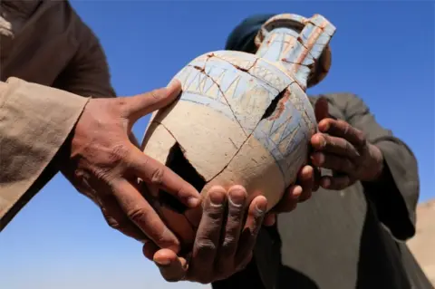 Reuters Two men hold a pieced-together earthen vase.