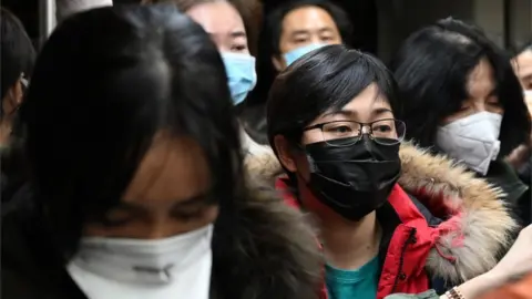 Getty Images Passengers from international flights wear protective face masks as they walk to the arrivals area at Beijing airport