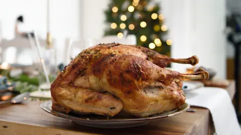 Getty Images A roast turkey on a silver plate on a table, with a blurry shape of a christmas tree in the background