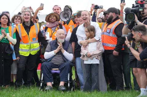 PA Media Michael and Emily Eavis open the gates to Glastonbury Festival, surrounded by stewards in high-vis jackets