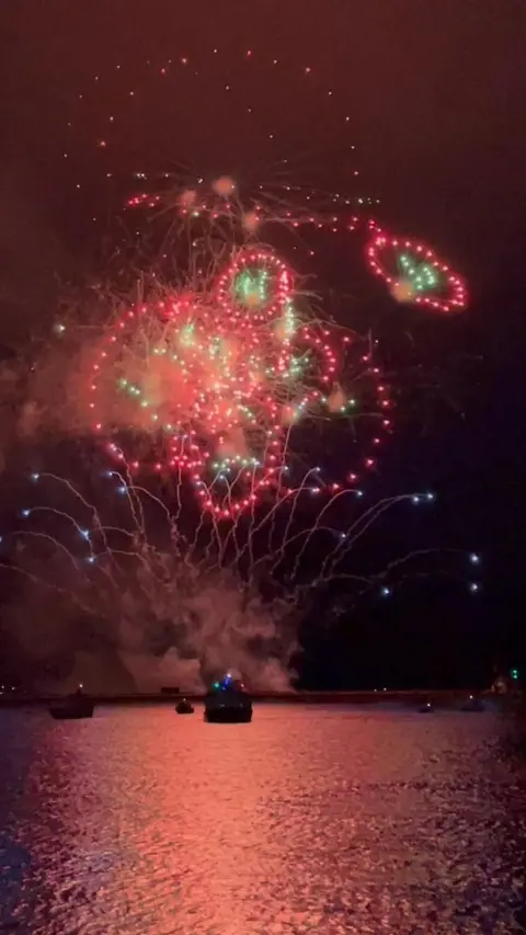 Red and green fireworks in the night sky over the sea. 