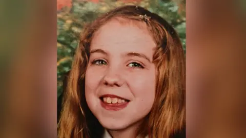 Family handout A childhood photo of a young Natalie McNally smiling at the camera. She has long, reddish blonde hair held back from her face with a clip. 
