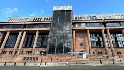 An imposing court building made from smooth red stones and columns with large dark windows.