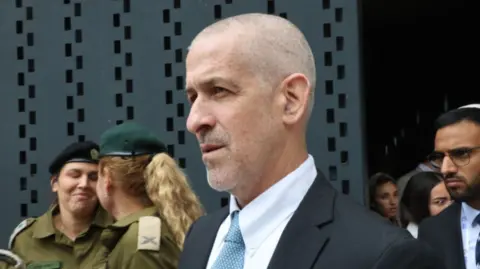 Getty Images Ronen Bar wearing a black suit and blue patterned tie