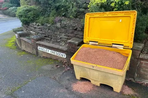 A full grit bin next to a road sign which reads: WINDLEY CRESCENT