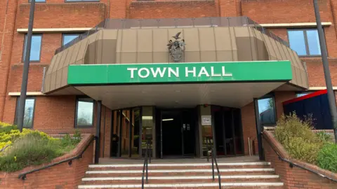 The outside of Redditch Borough Council's headquarters - a large brick building with a green sign that says 'town hall'. 