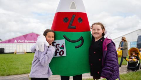 Two young girls pose for a photo with the Urdd mascot, Mister Urdd.