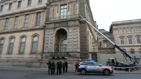 DIMITAR DILKOFF/AFP via Getty Images A polícia está na base do Louvre, com a escada mecânica estendendo-se até lá atrás deles.