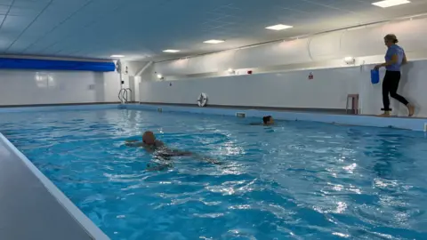 Tom Jackson/BBC A swimming pool with two people swimming in it.