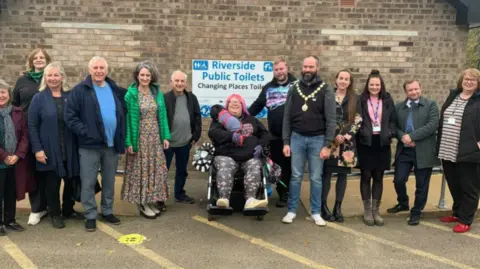 Cambridgeshire County Council A group of people lined up by a wall with a sign "Riverside Public Toilets".