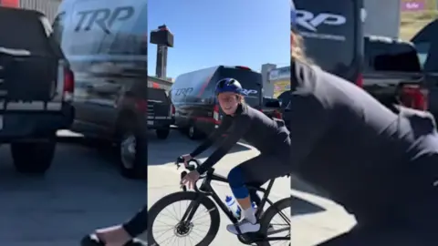 Woman on a bike wearing a helmet, glasses and cycling clothes.
