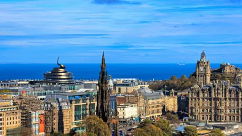 Getty Images A picture of the central Edinburgh skyline, with buildings including the Scotsman Hotel and Scott Monument standing out against a blue sky over the blue water of the Forth